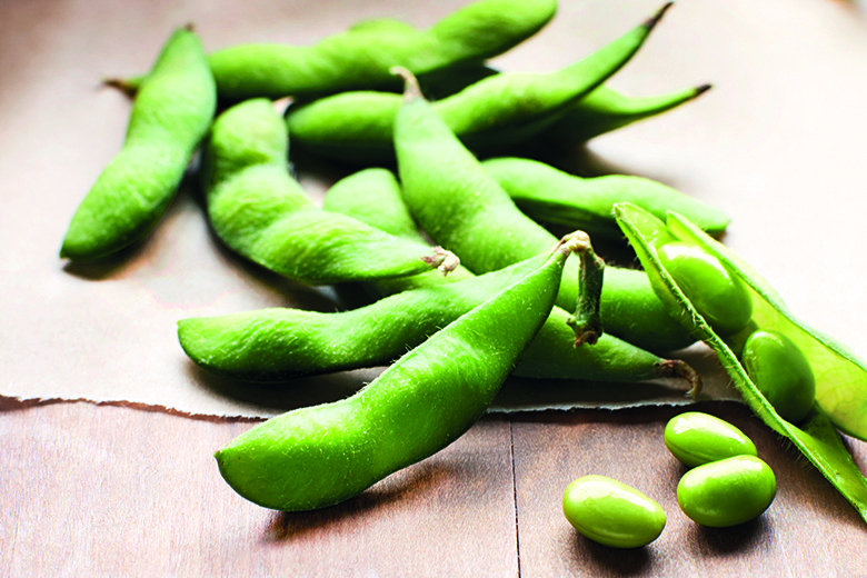 Shelled edamame on a wood background with a few shelled beans