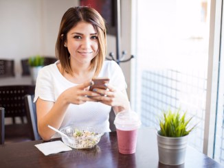 Woman using smartphone while eating salad and smoothie at cafe