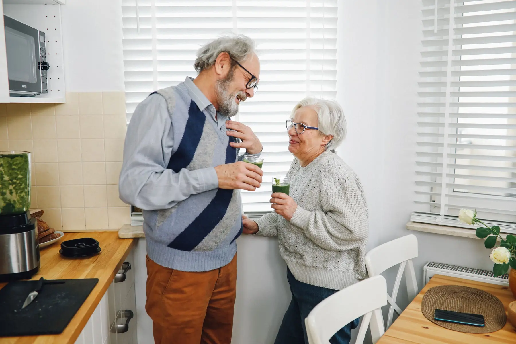 Happy senior couple enjoying refreshing green smoothies together in a cozy kitchen.