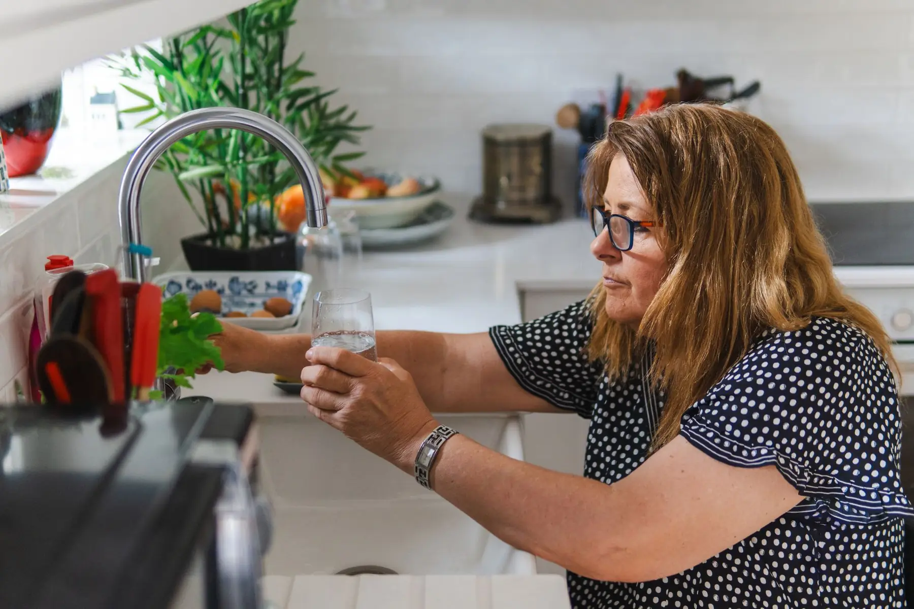 A middle-aged woman filling a glass with water in a modern kitchen setting