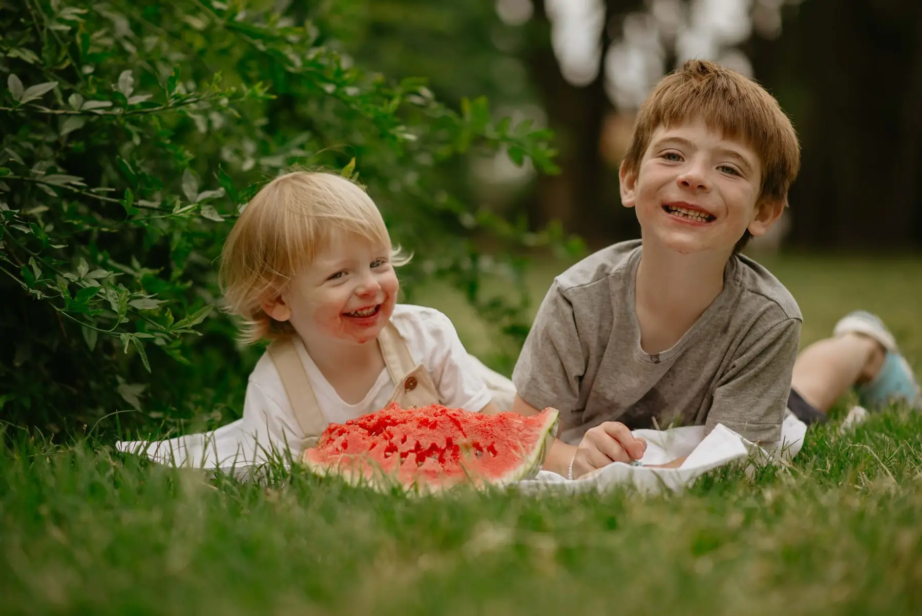 Two children smiling and enjoying watermelon on a summer day outdoors