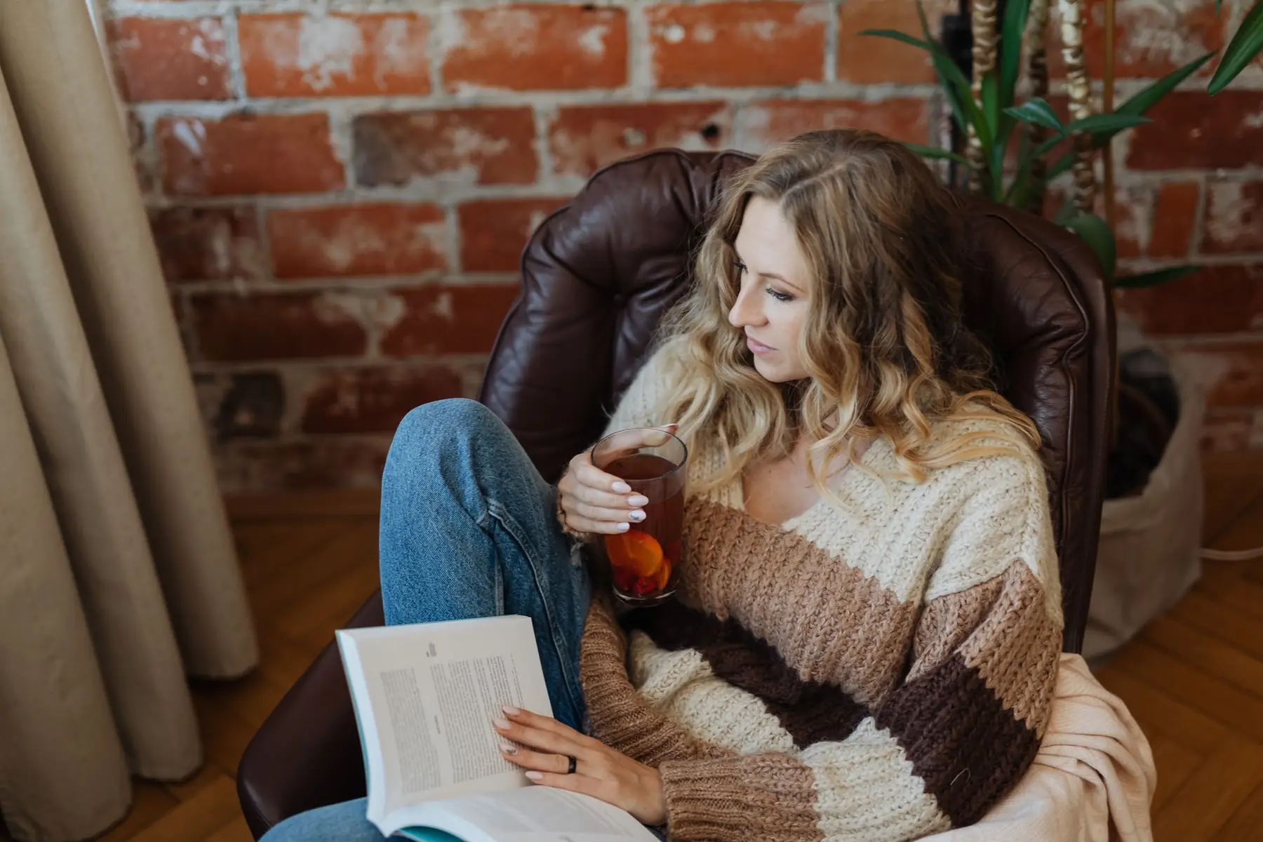 A woman enjoying a book and a cup of tea in a stylish armchair