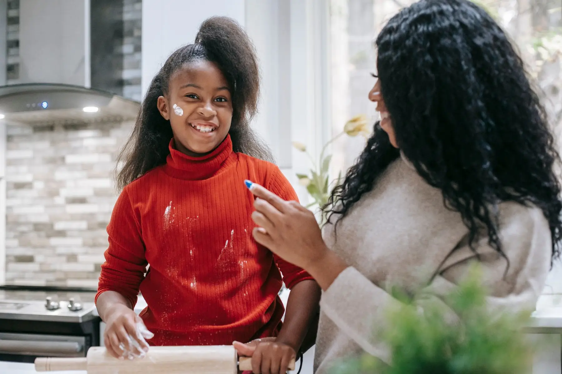 Happy black child with flour on face and rolling pin near crop parent at