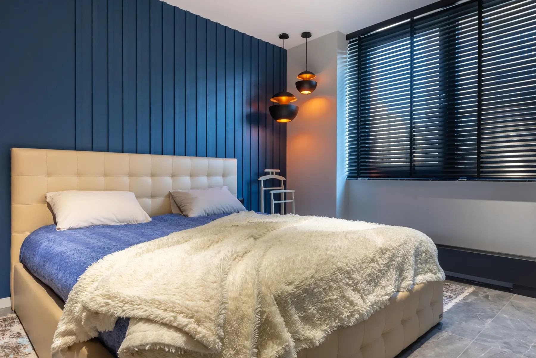 Modern bedroom interior with blanket and pillows on bed against lamps and jalousie in house