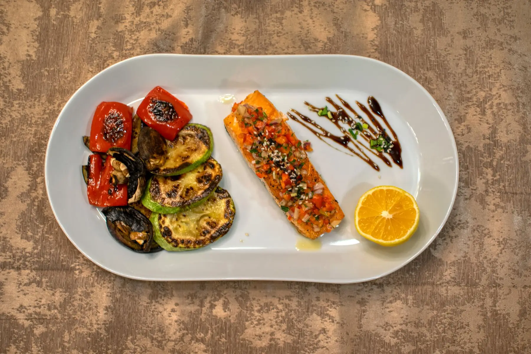 Gourmet grilled salmon served with roasted vegetables and lemon slice on a white plate