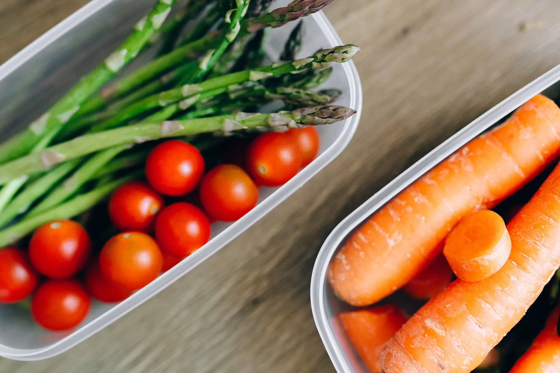 Close-up of fresh asparagus, cherry tomatoes, and carrots in plastic containers on a wooden