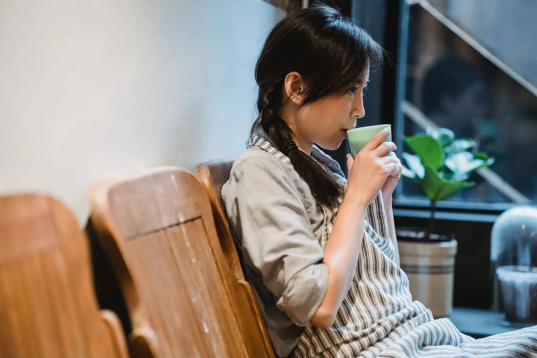 A woman sits enjoying a coffee, embracing relaxation by a window seat indoors