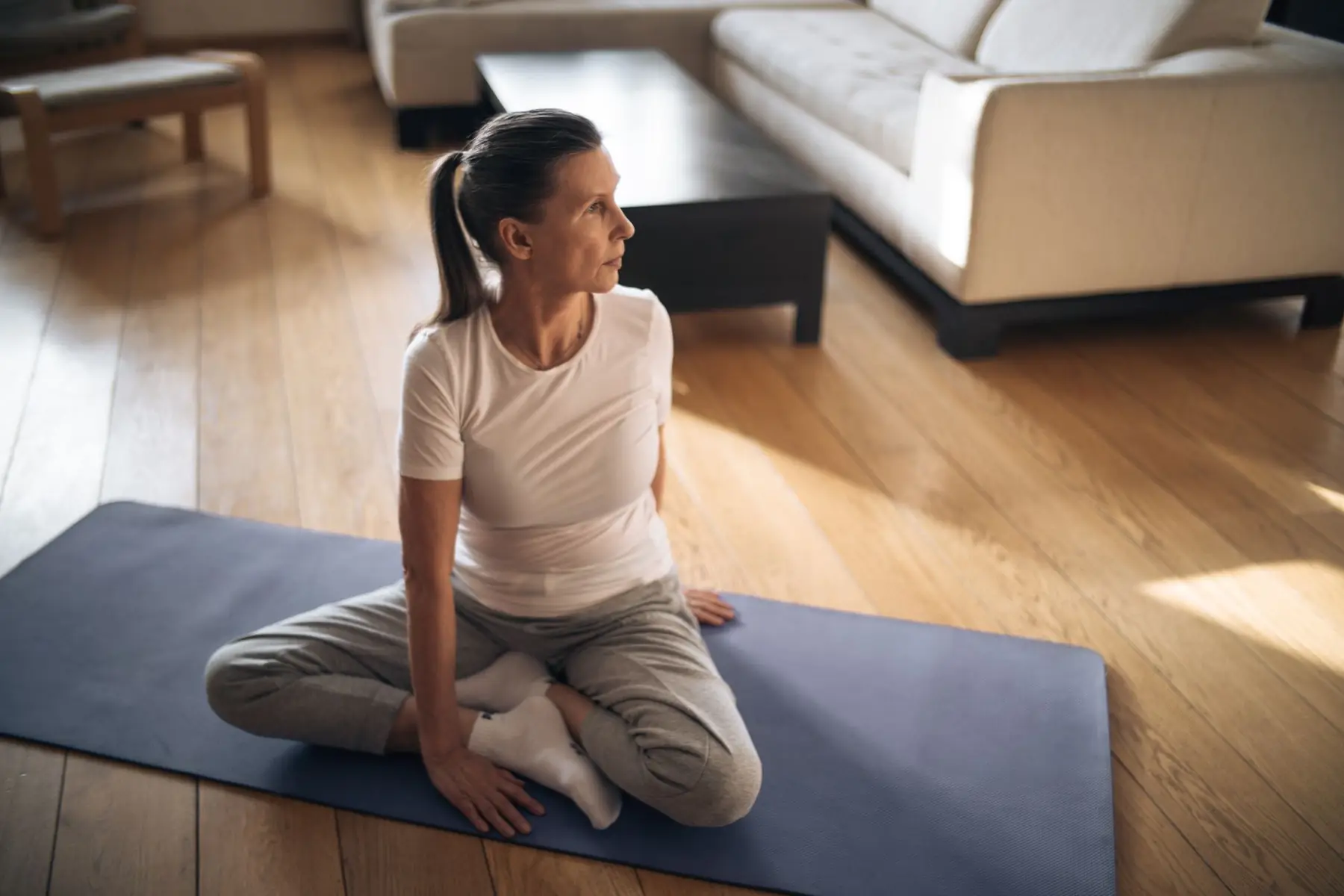Elderly woman in activewear practicing yoga at home on a sunny day