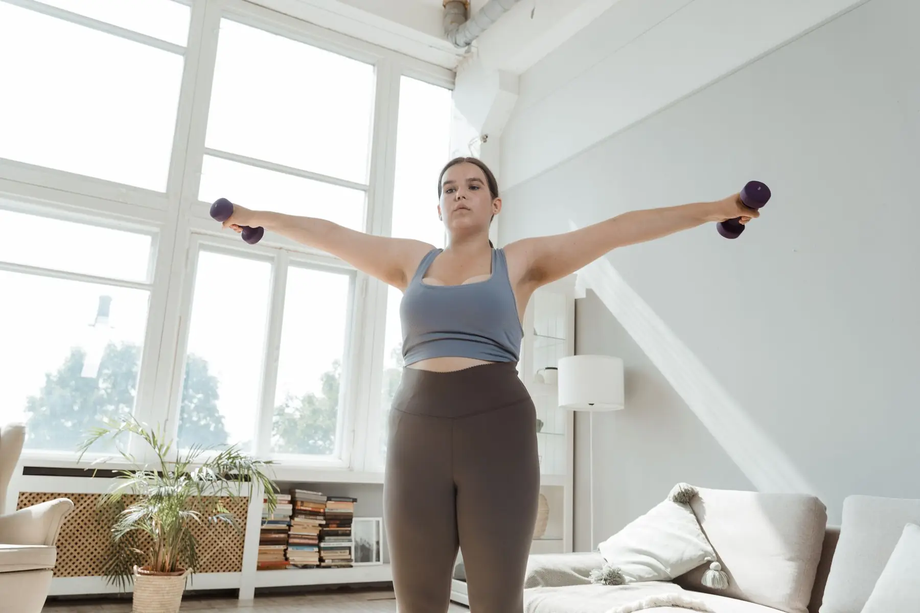 Determined young woman in activewear lifting dumbbells indoors for fitness