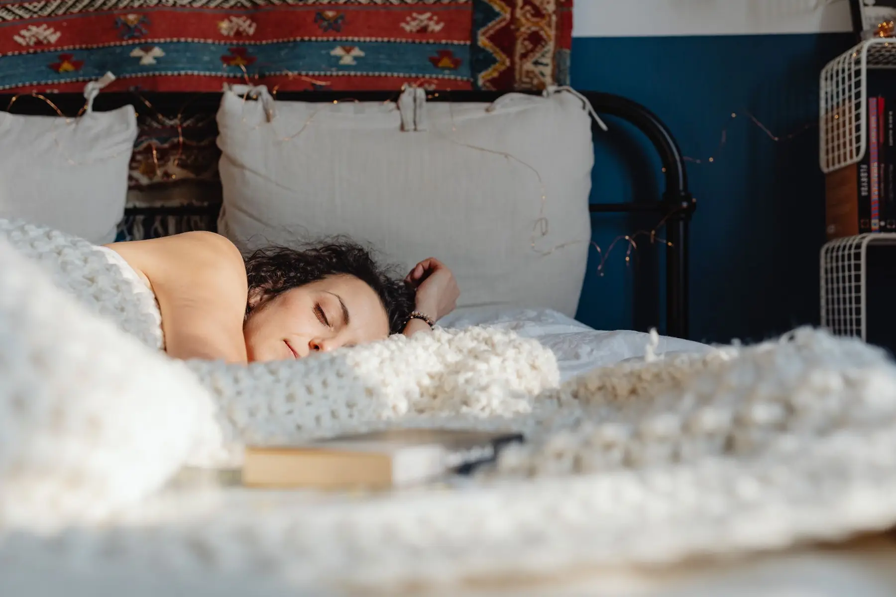 A woman peacefully sleeping on her side in a cozy, sunlit bedroom with decorative