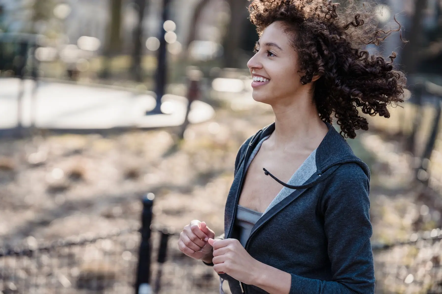 Side view of young African American female smiling while running in park against blurred