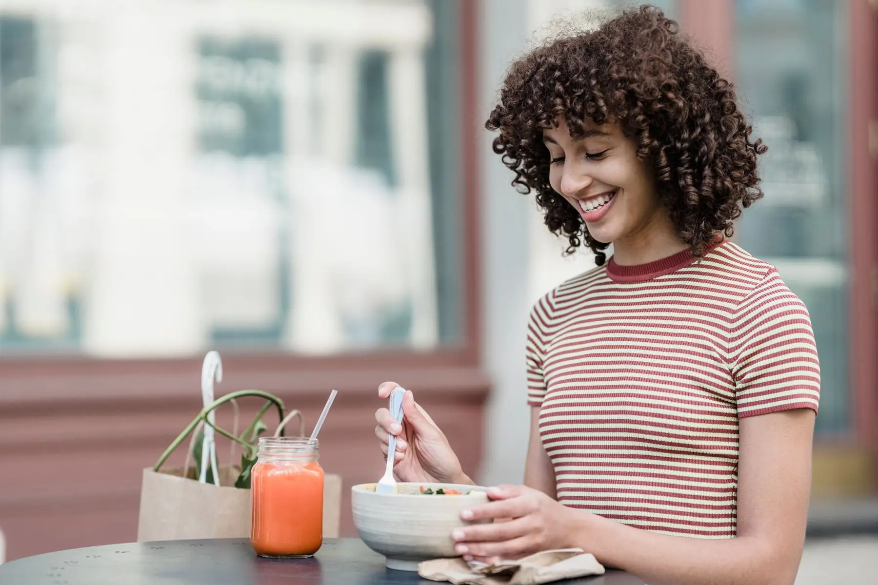 Cheerful young female with bowl of yummy food and jar of refreshing beverage sitting