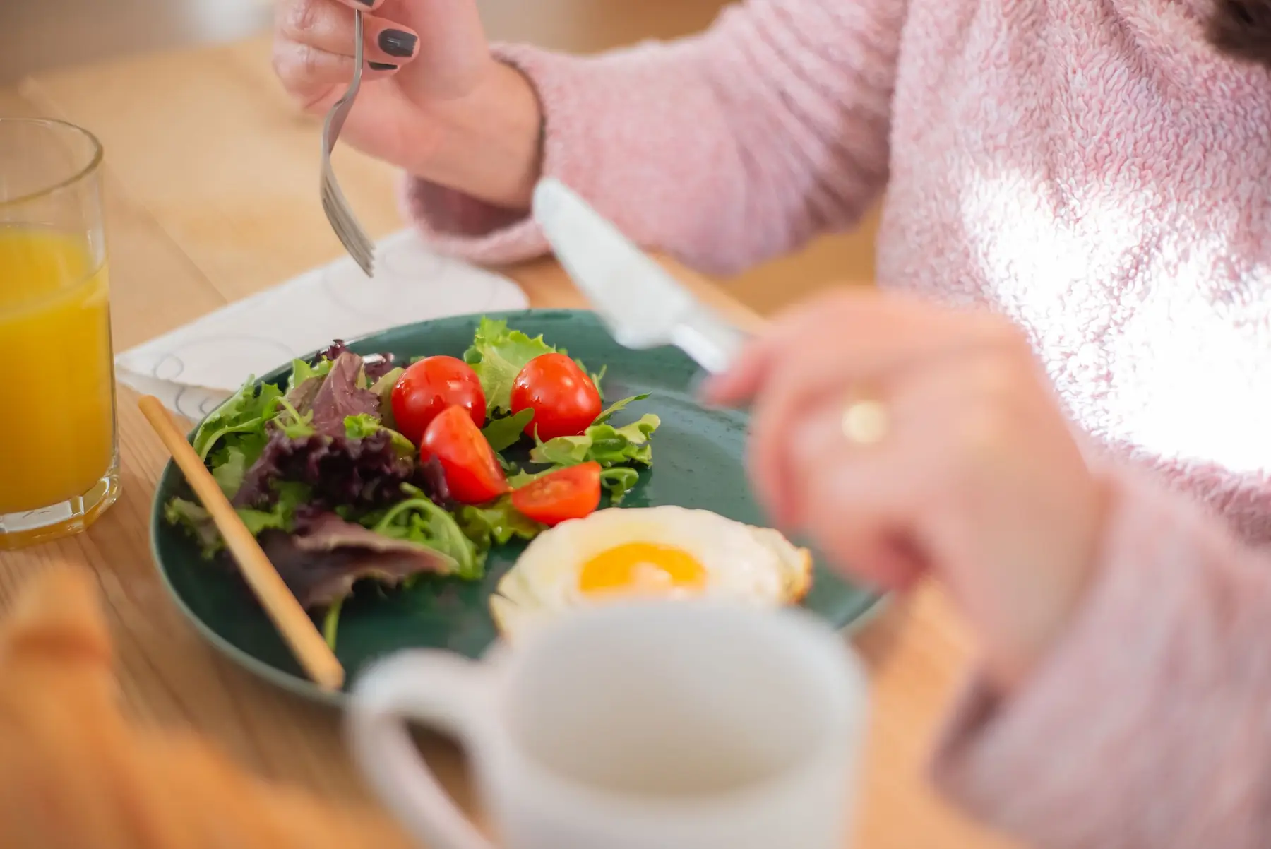 A woman enjoys a protein breakfast of egg and salad at a wooden table