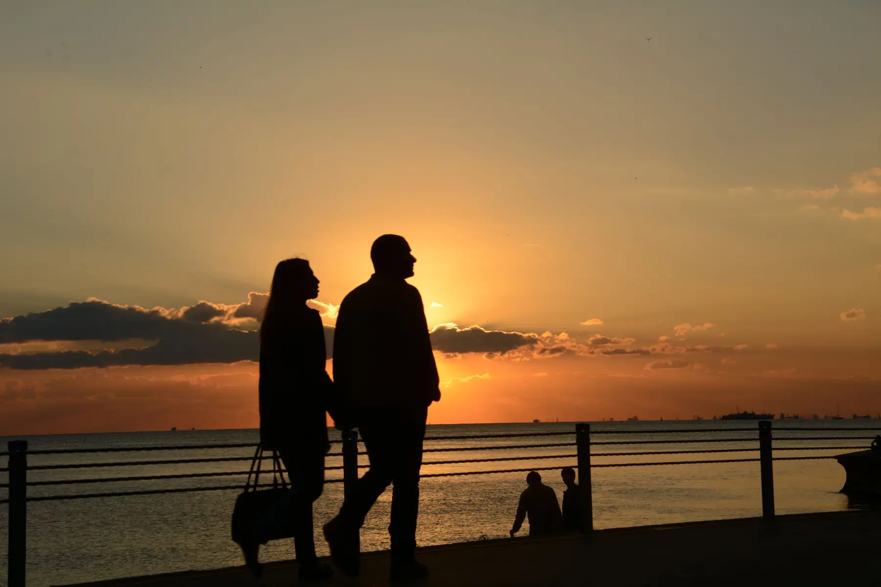 A couple walks together at sunset along a seaside railing