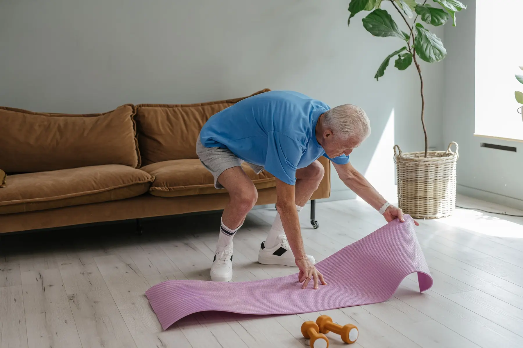 An older man sets up a mat and light weights in a sunny room