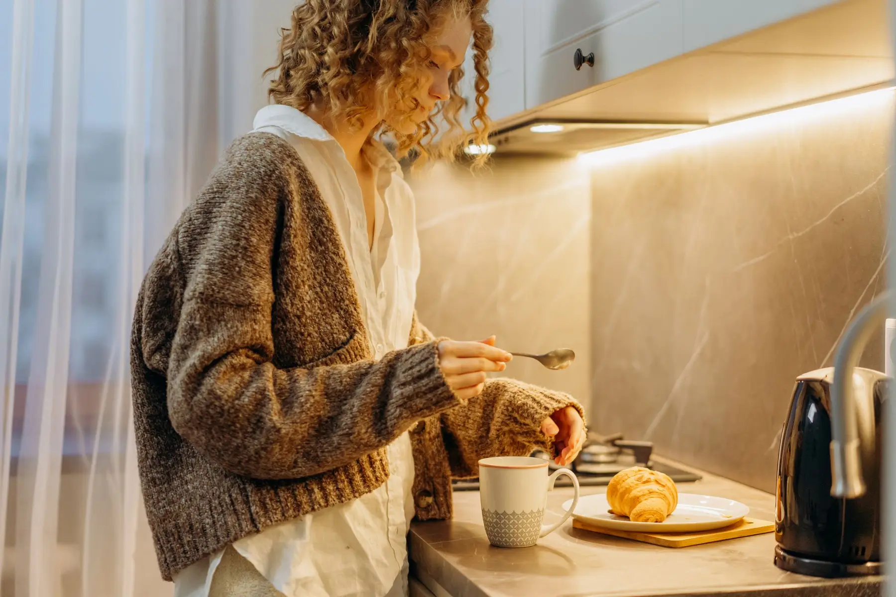 A woman in a cozy cardigan prepares tea and a small snack