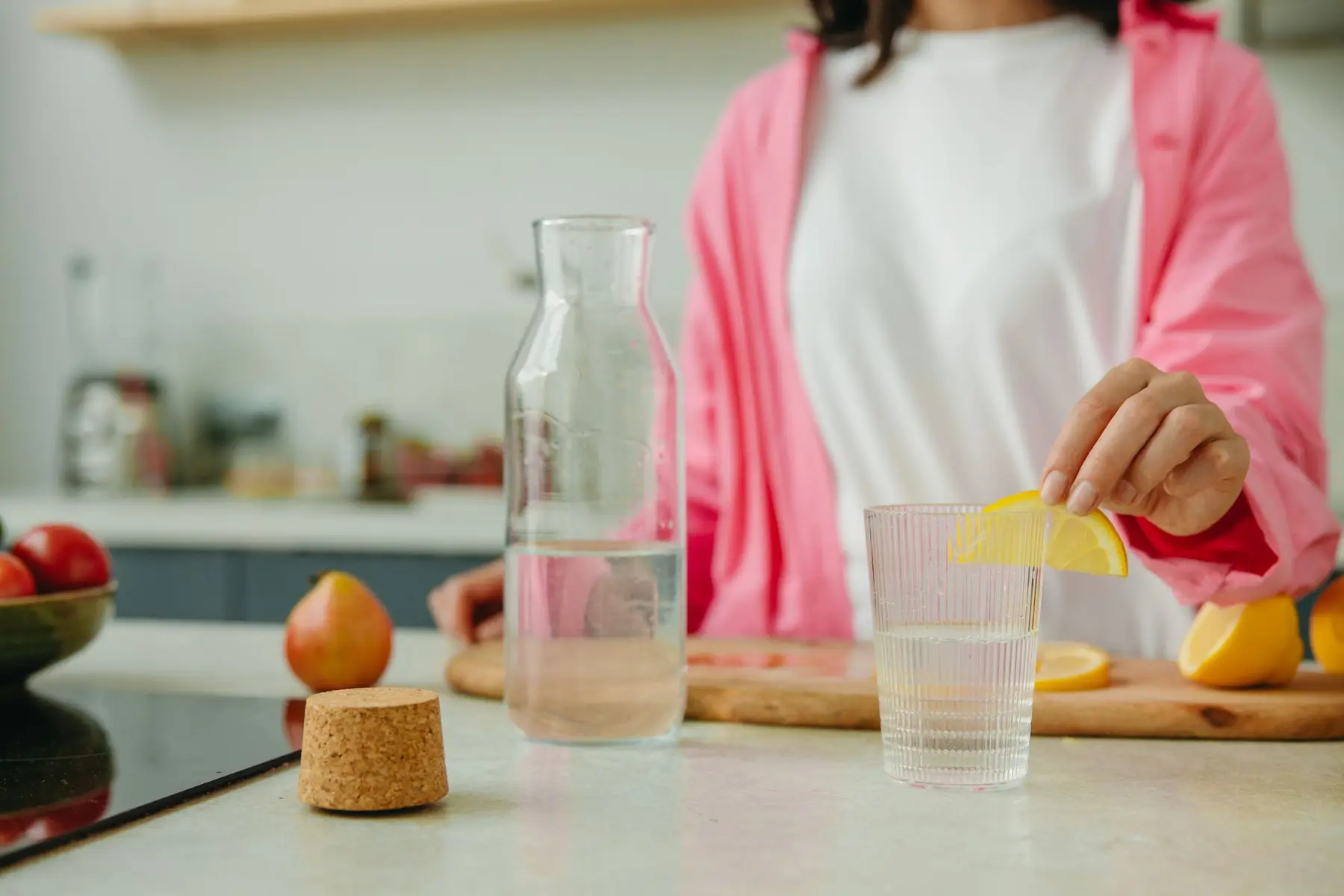 A woman adds a lemon slice to a glass of water in a kitchen