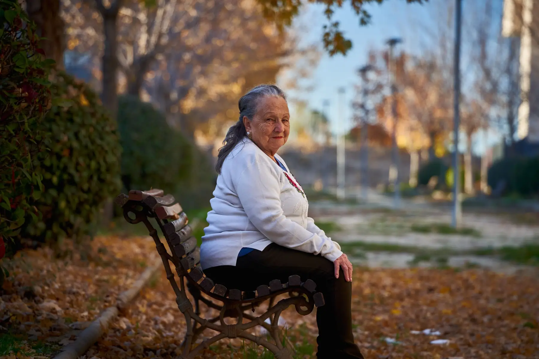 A woman in a white cardigan sits on a bench in warm autumn sun