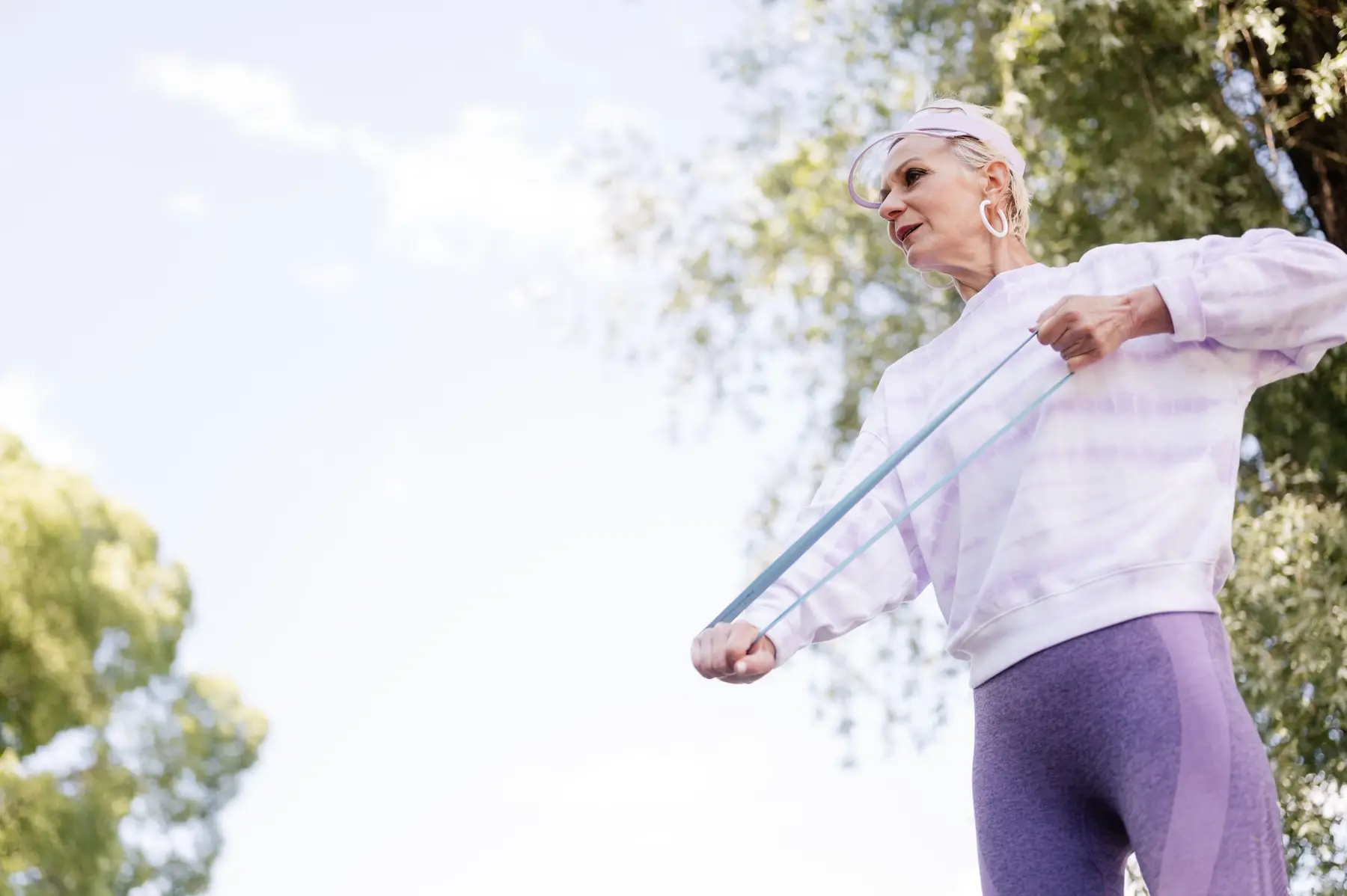 An older woman stretches a resistance band outdoors in soft daylight