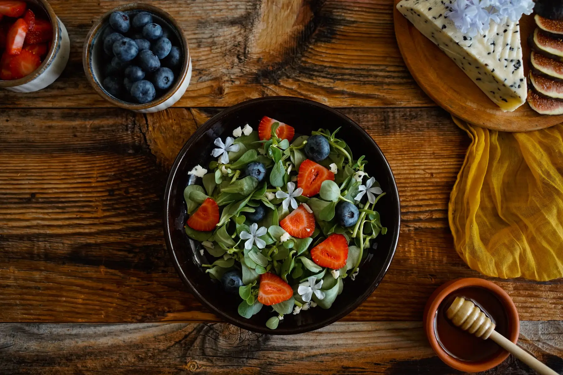 A bowl of leafy salad with strawberries on a warm wooden table