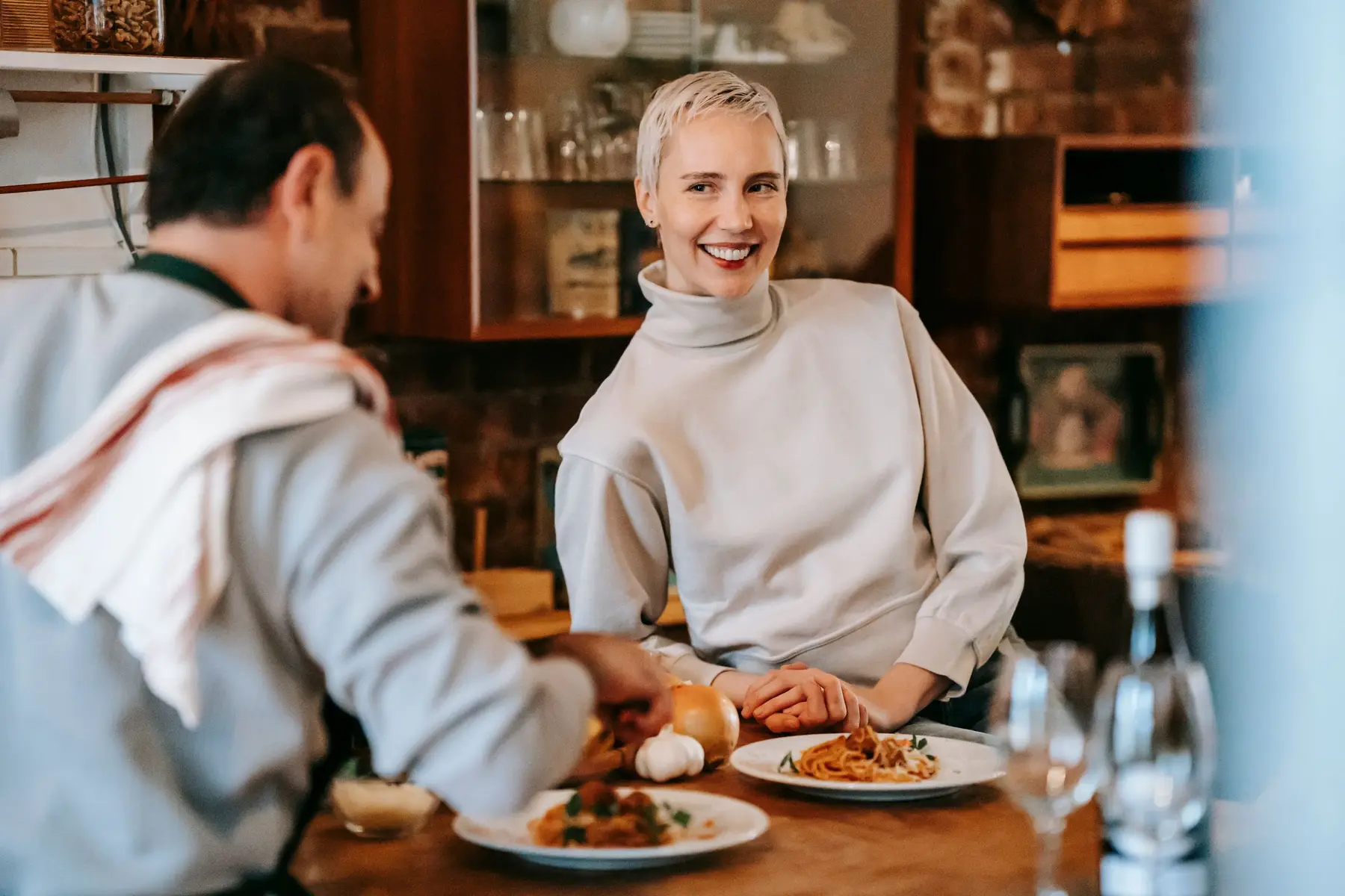 A smiling couple plate a simple pasta dinner in a warm brick kitchen