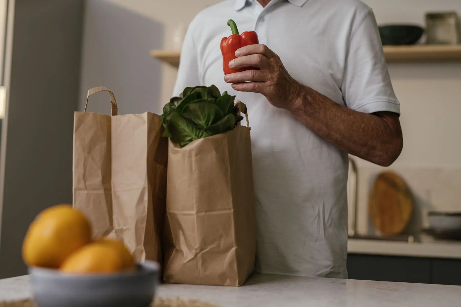 An older man unpacks groceries from a paper bag in a warm kitchen