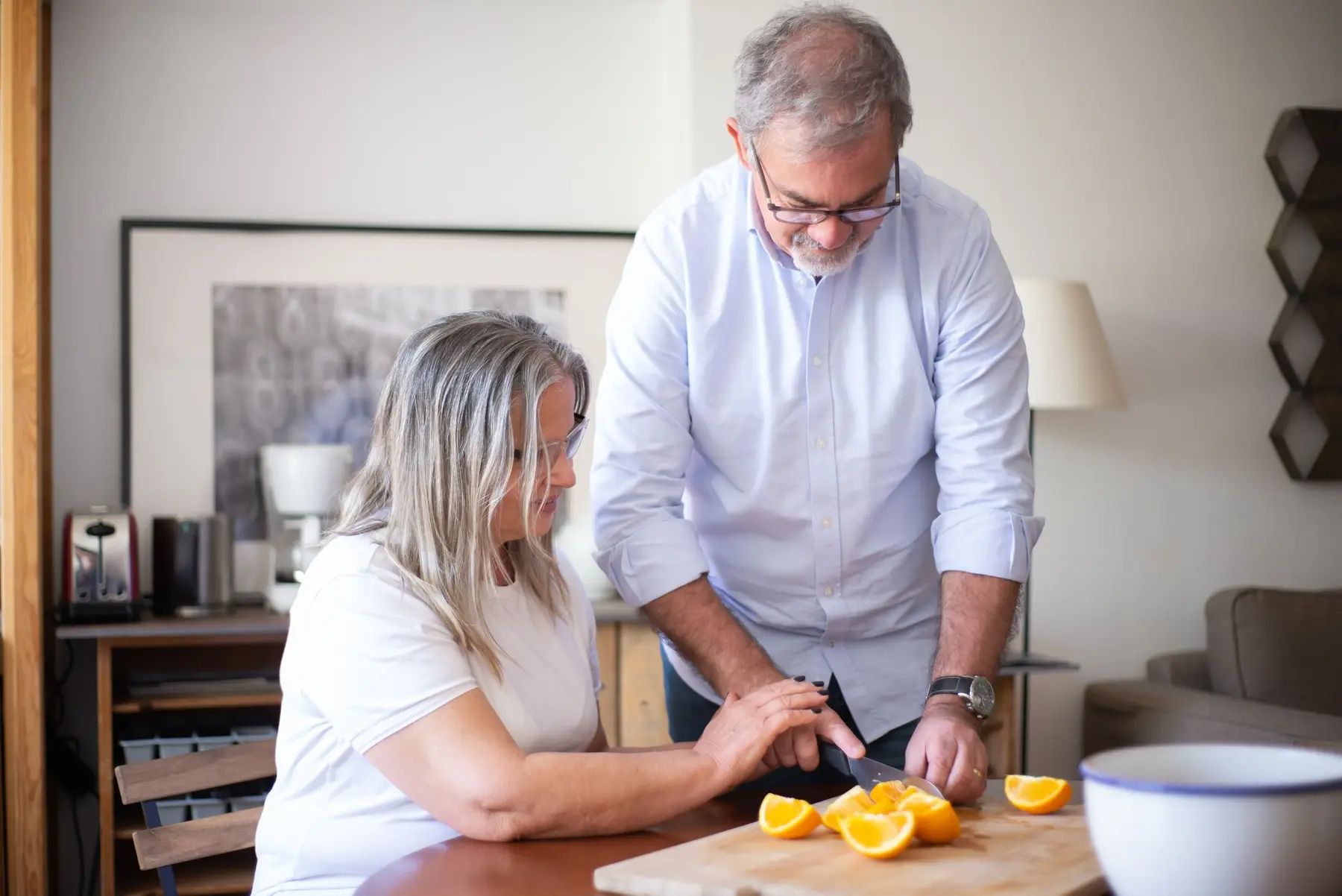 An older couple slice fresh oranges together in a bright kitchen