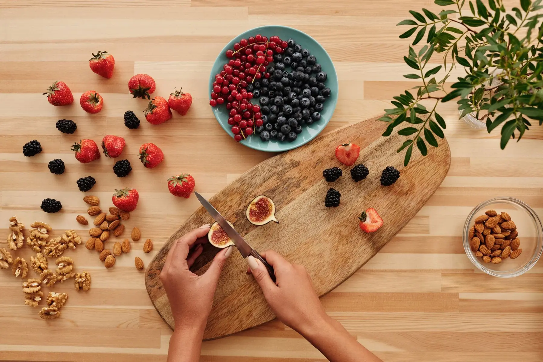 Overhead shot of fresh fruits, nuts, and hands preparing ingredients on a wooden board