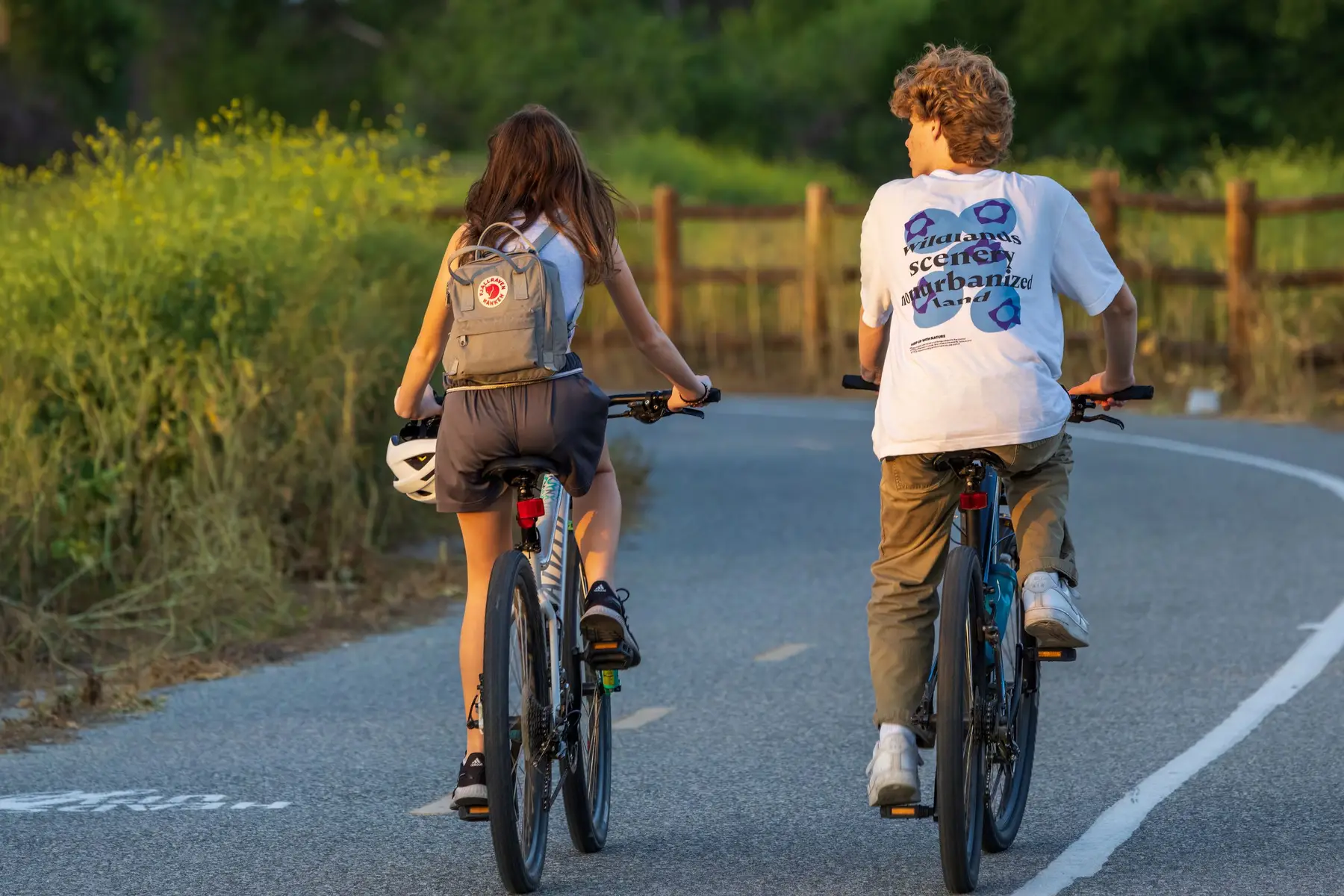 Two friends ride bikes together on a quiet road in warm evening light
