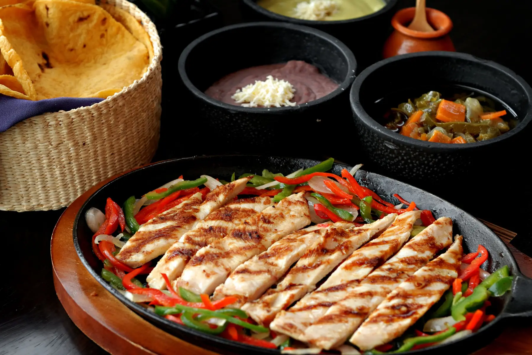 Grilled chicken strips with peppers and onions in a skillet beside tortillas