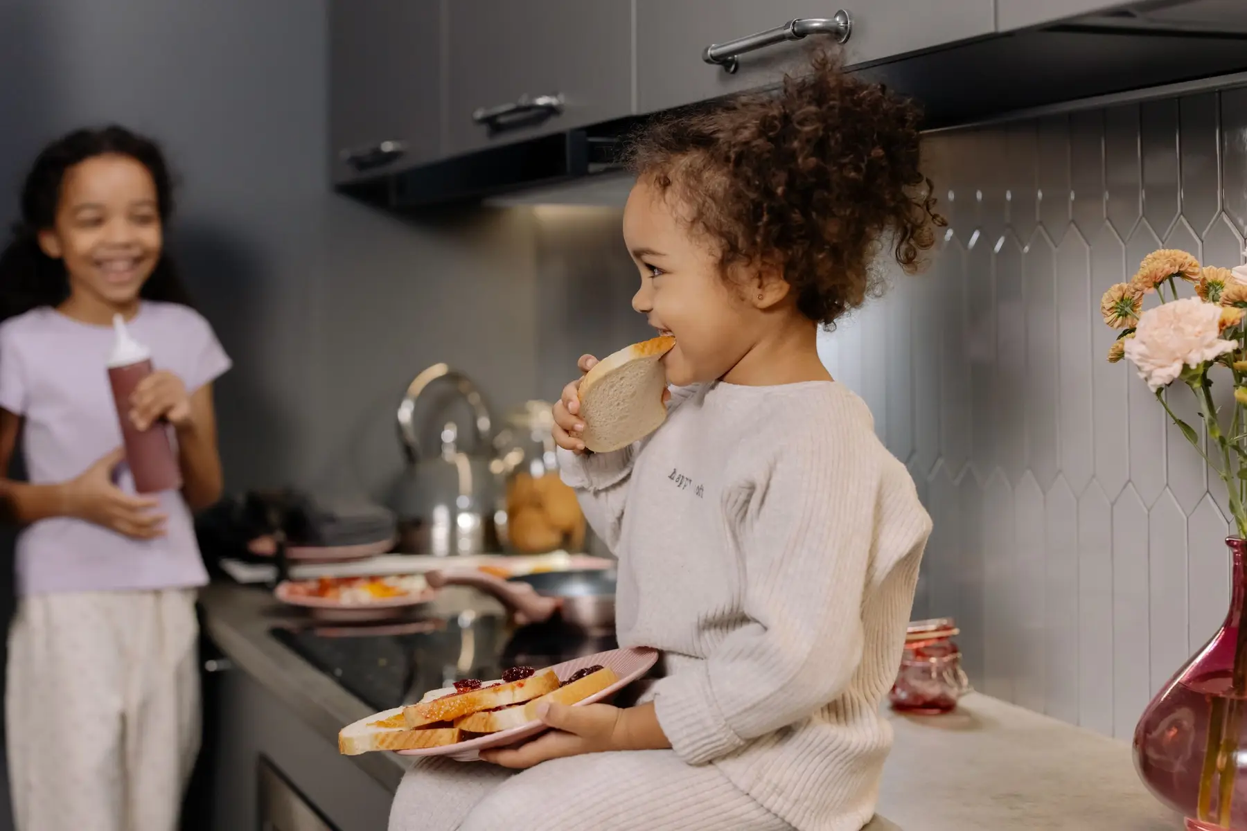 Two smiling children share a snack in a cozy kitchen