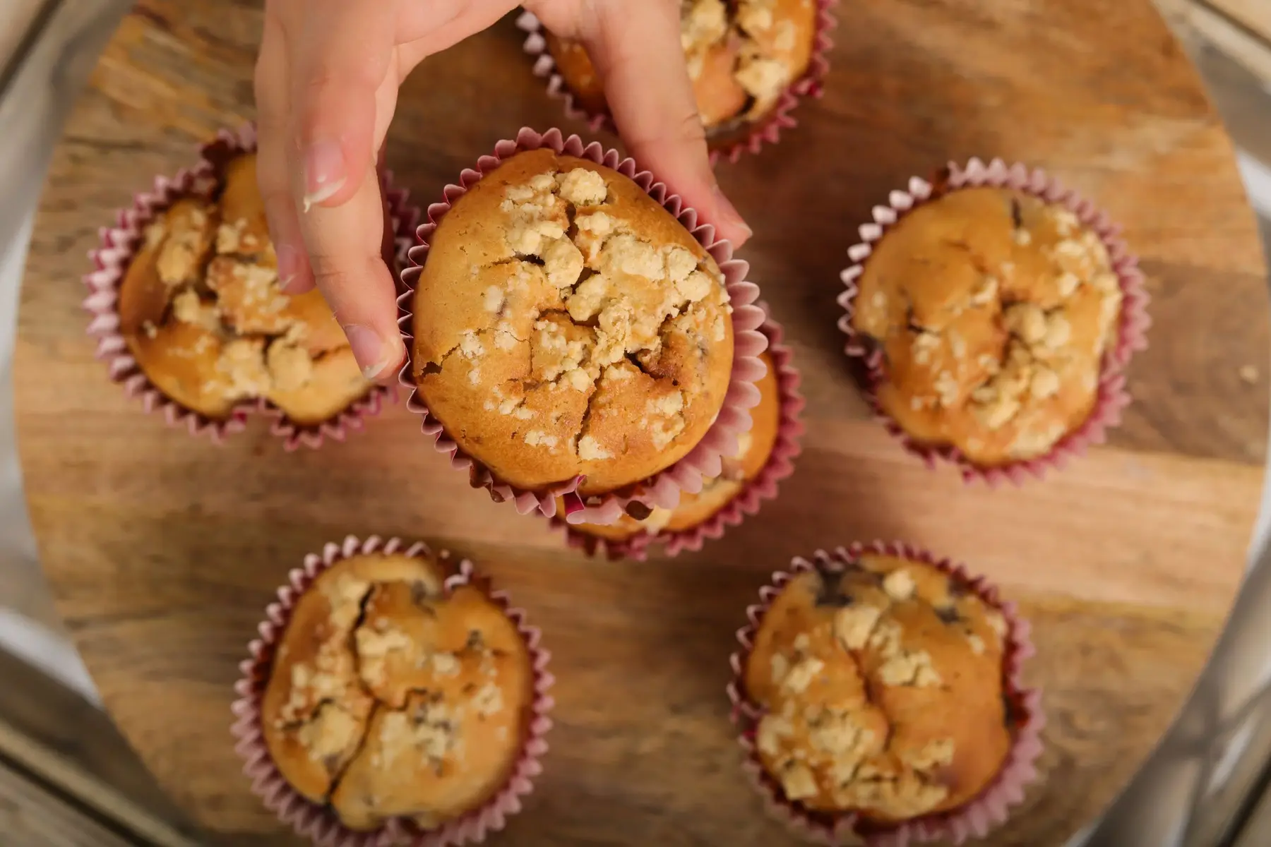Hands lift golden baked oat cups from a wooden board