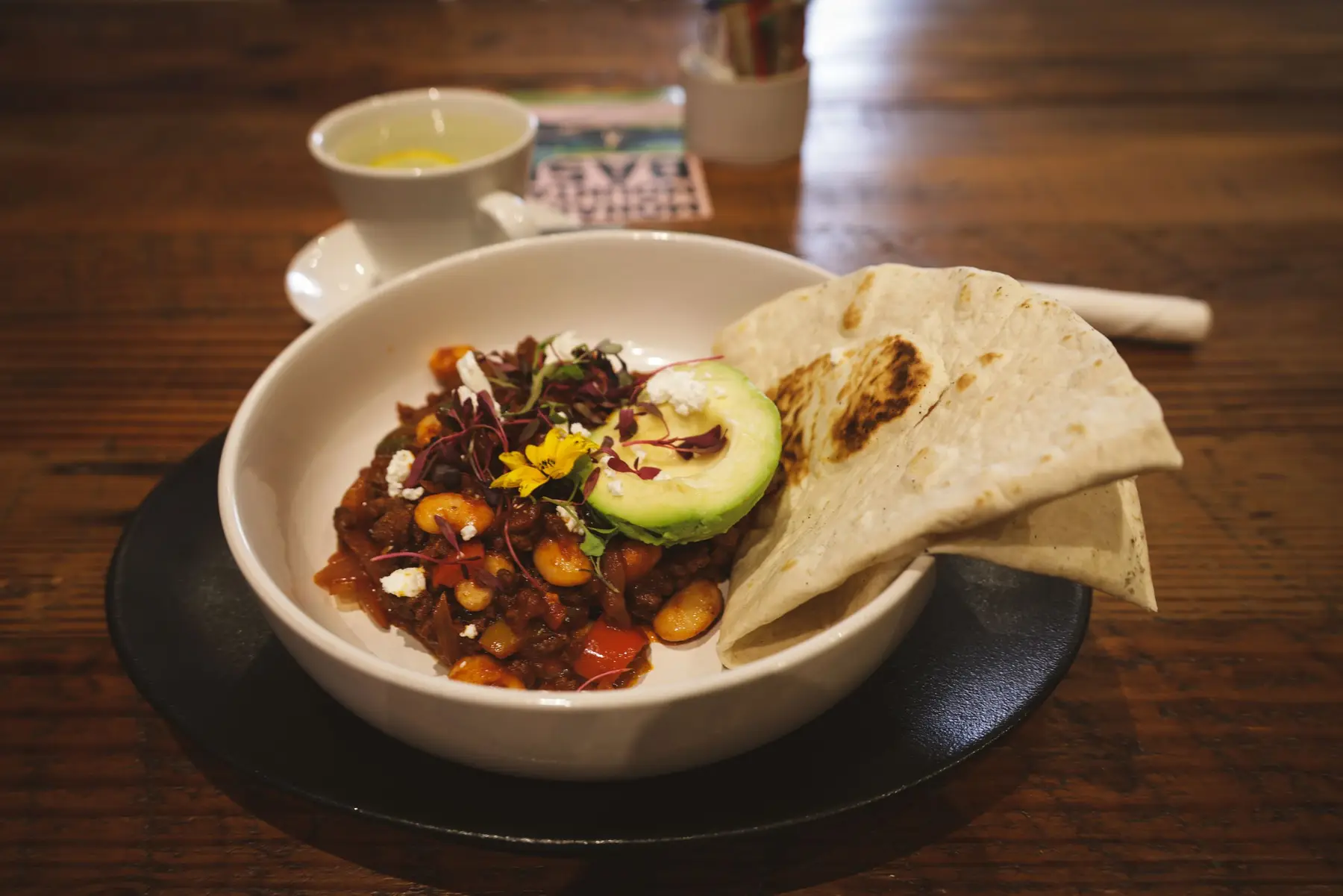 A bowl of hearty bean chili with avocado and warm flatbread