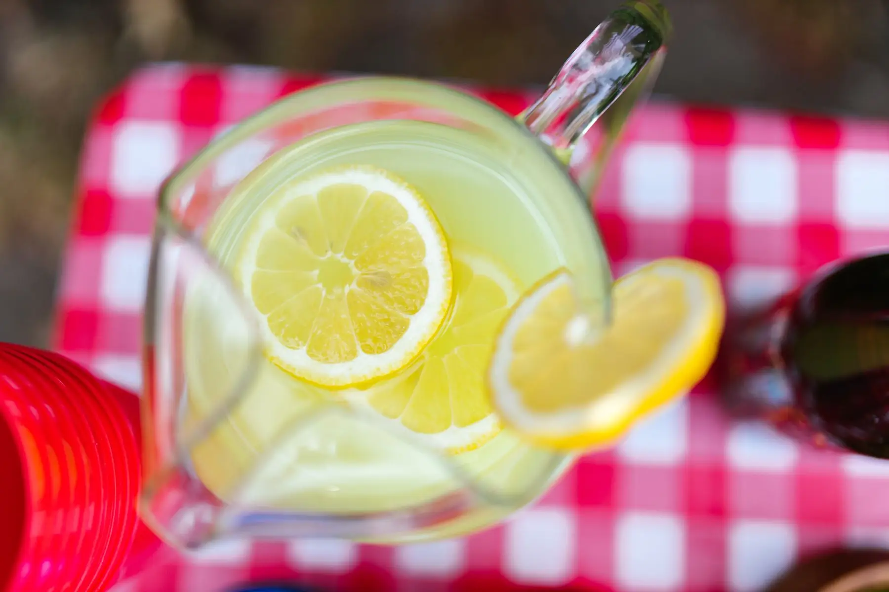 A top-view of lemonade with lemon slices in a pitcher on a checkered picnic