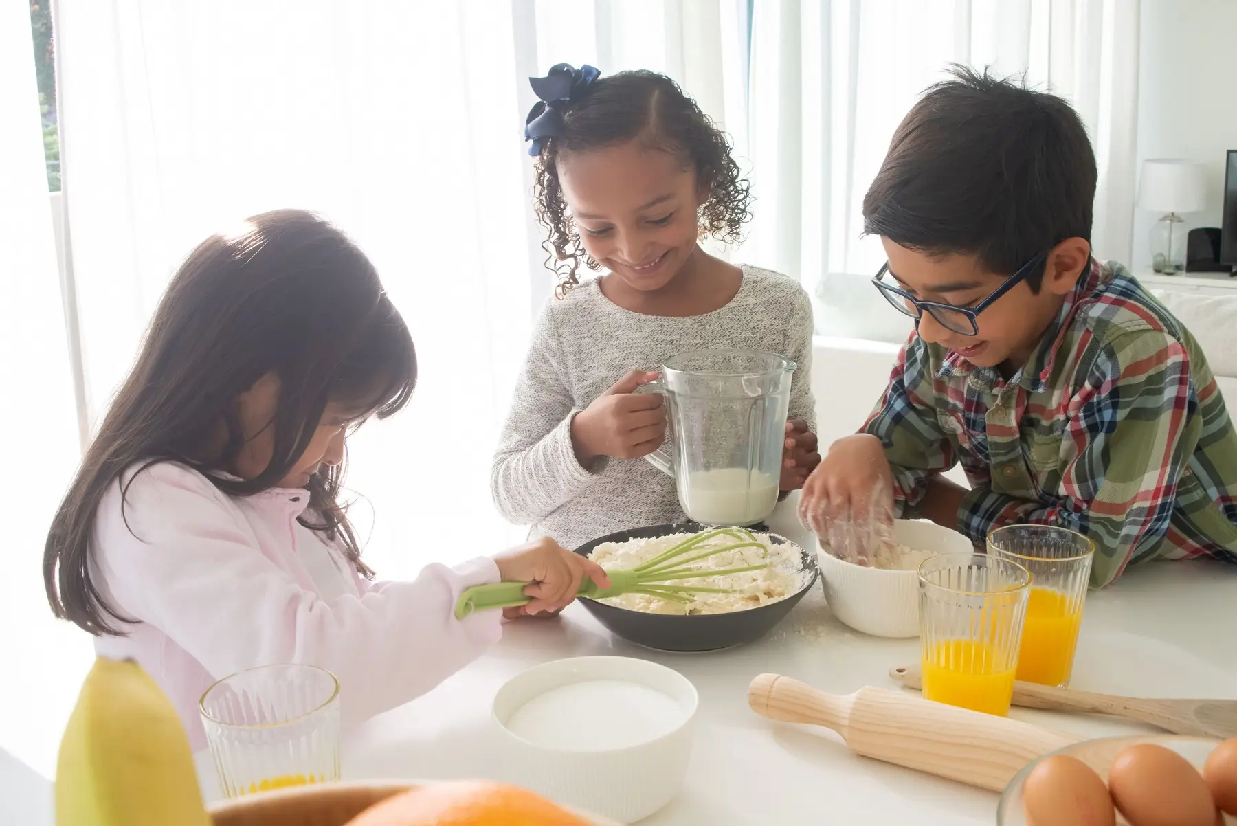 Children prepare a snack together at a bright kitchen table