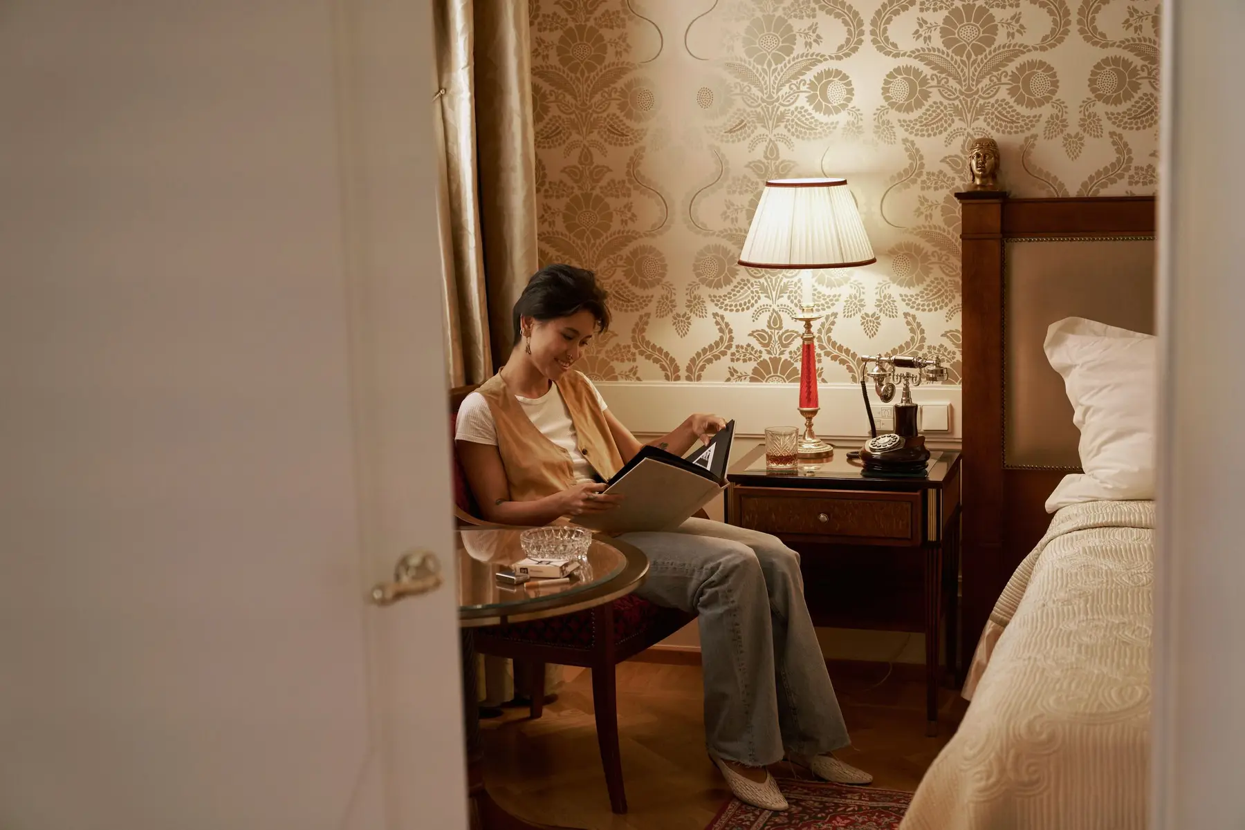 A woman reads in a quiet lamplit bedroom in the evening
