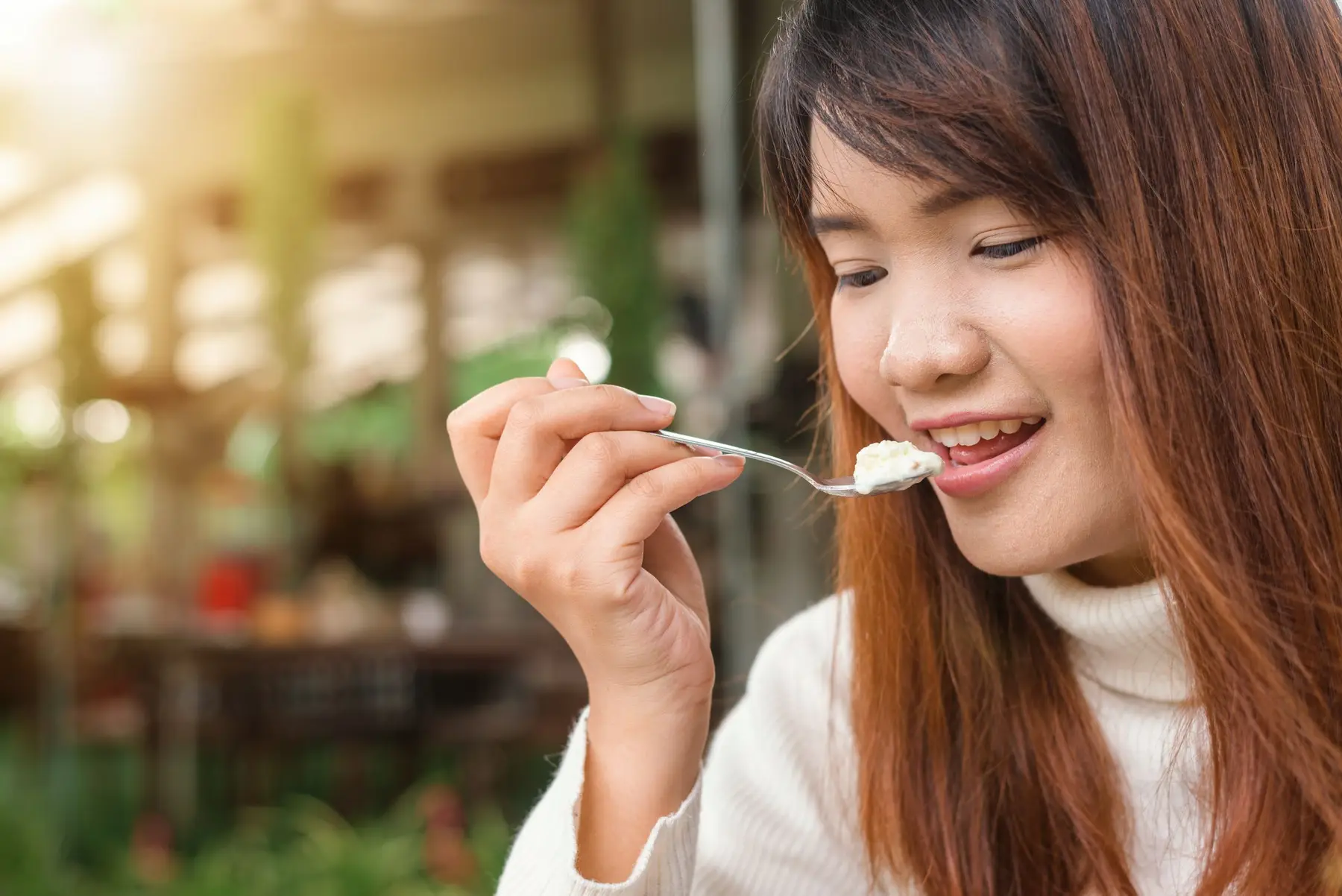 A smiling woman enjoys a spoonful of yogurt in warm light