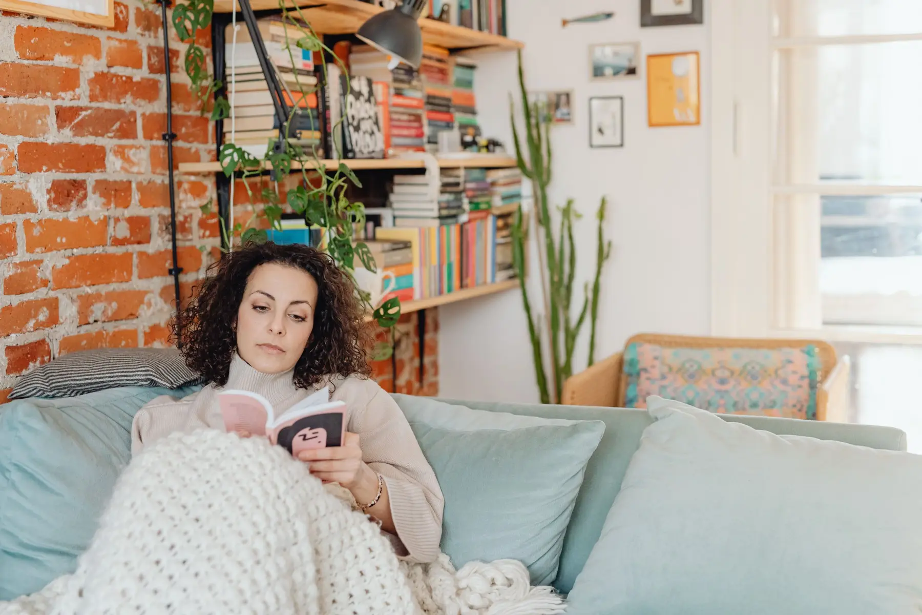 A woman reads a magazine under a soft blanket on a sofa