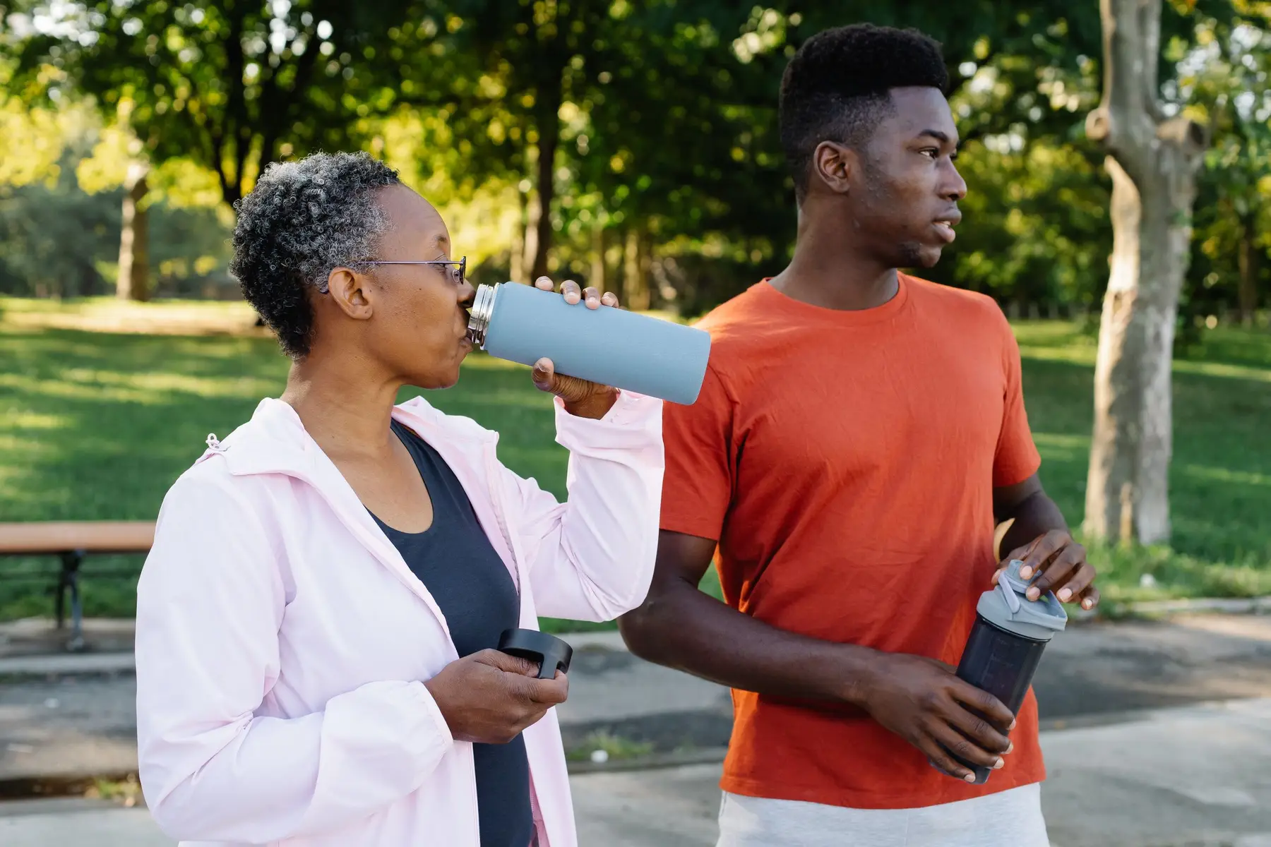 Two friends sip from water bottles during a walk in a sunny park