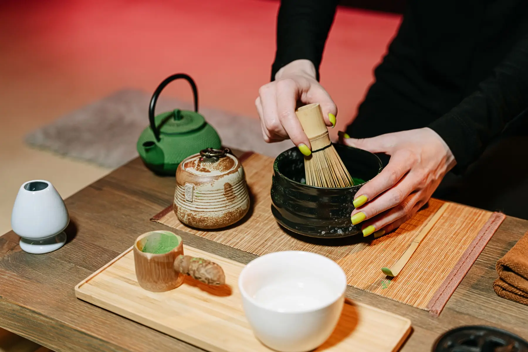 Hands whisk matcha in a bowl on a warm wooden table