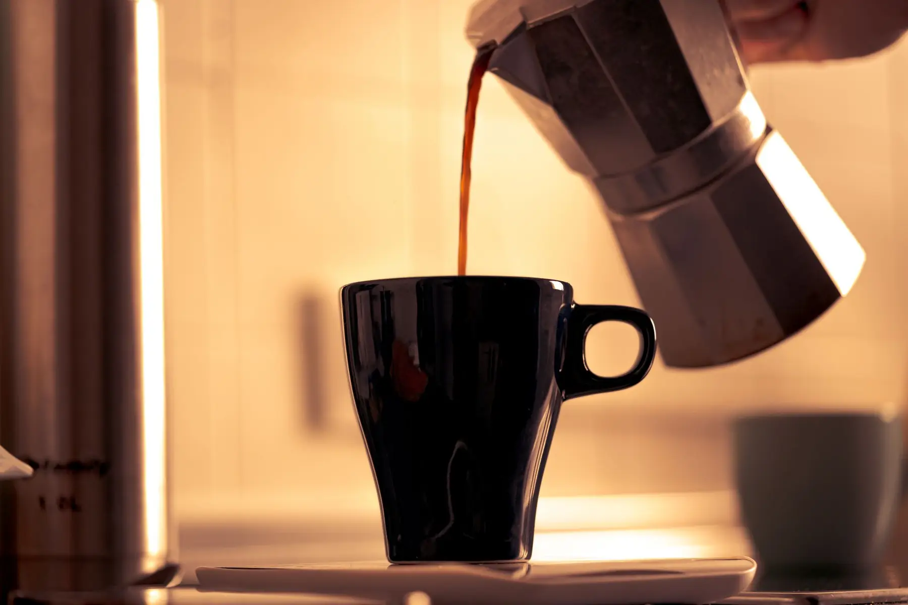 Warm morning coffee being poured into a cup from a classic moka pot