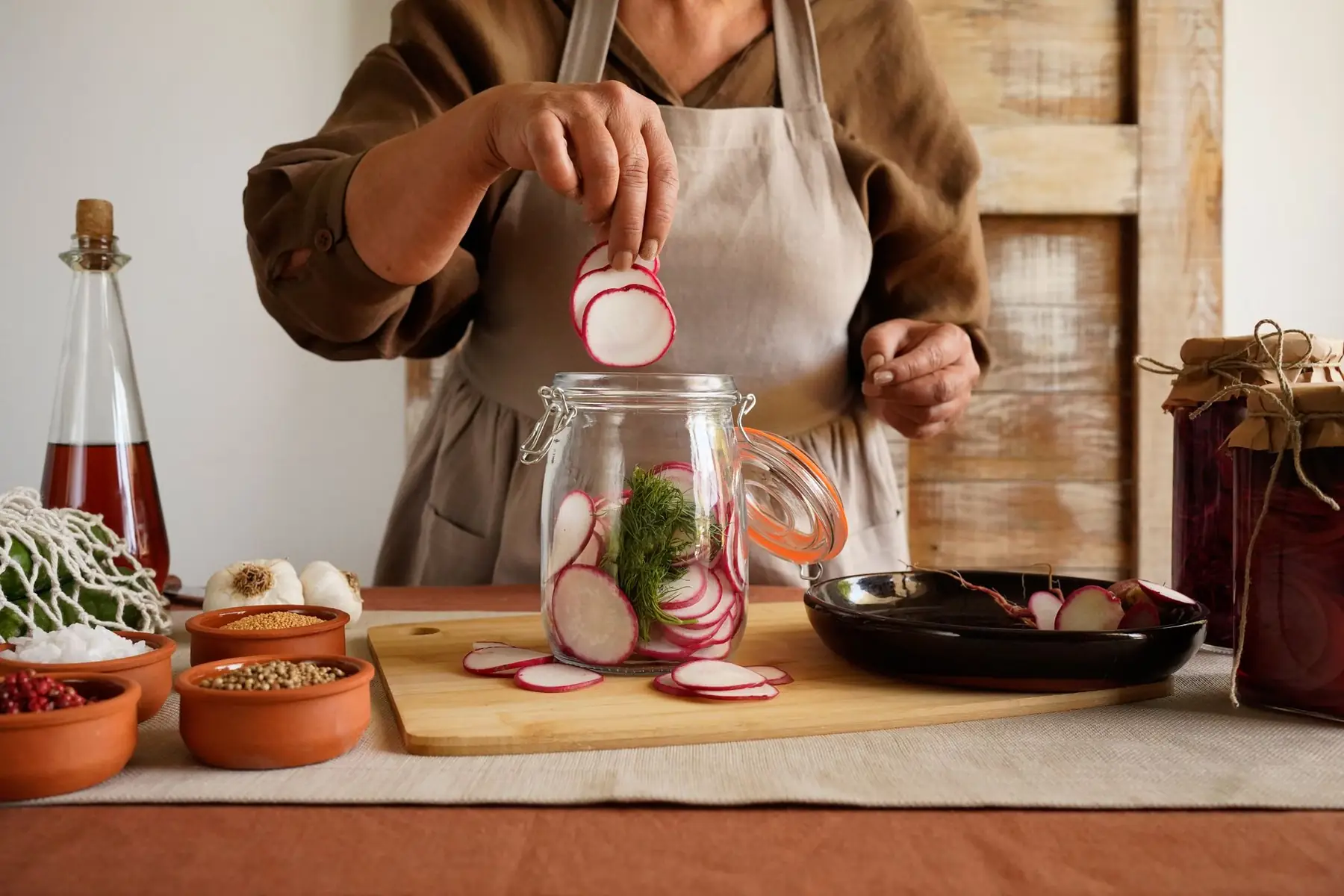 A woman preparing pickled radishes, showcasing ingredients in a rustic kitchen setting