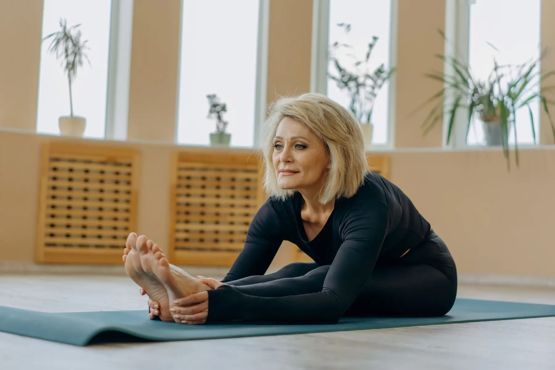 Elderly woman stretching on a yoga mat indoors, highlighting flexibility and wellness