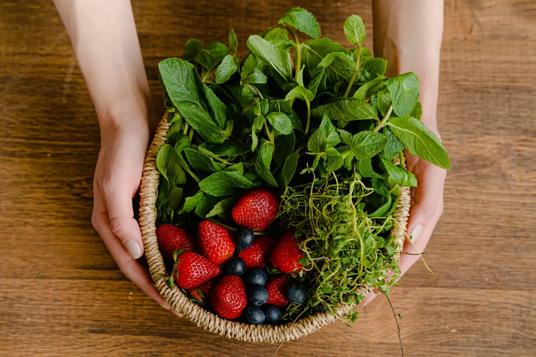 Top view of a basket filled with fresh strawberries, blueberries, and mint, held by