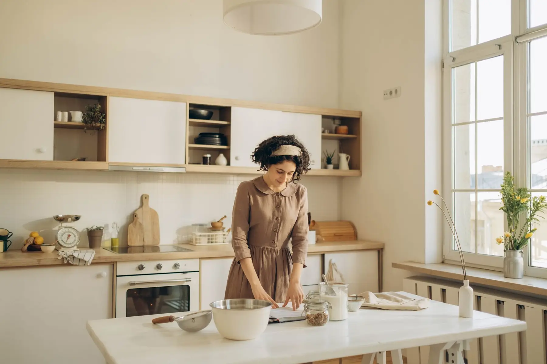A woman with curly hair prepares food in a bright and cozy home kitchen,
