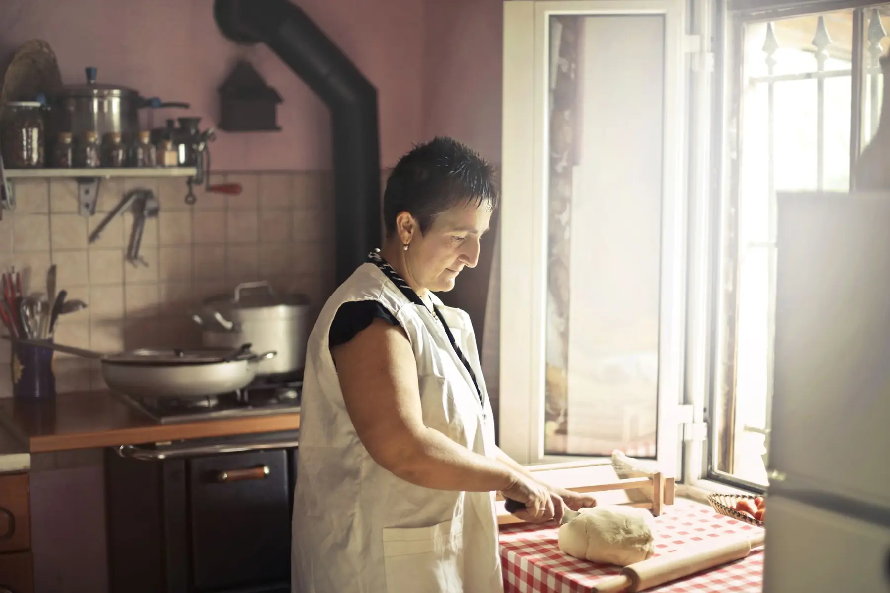 Woman in apron kneading dough by window in rustic kitchen with warm light