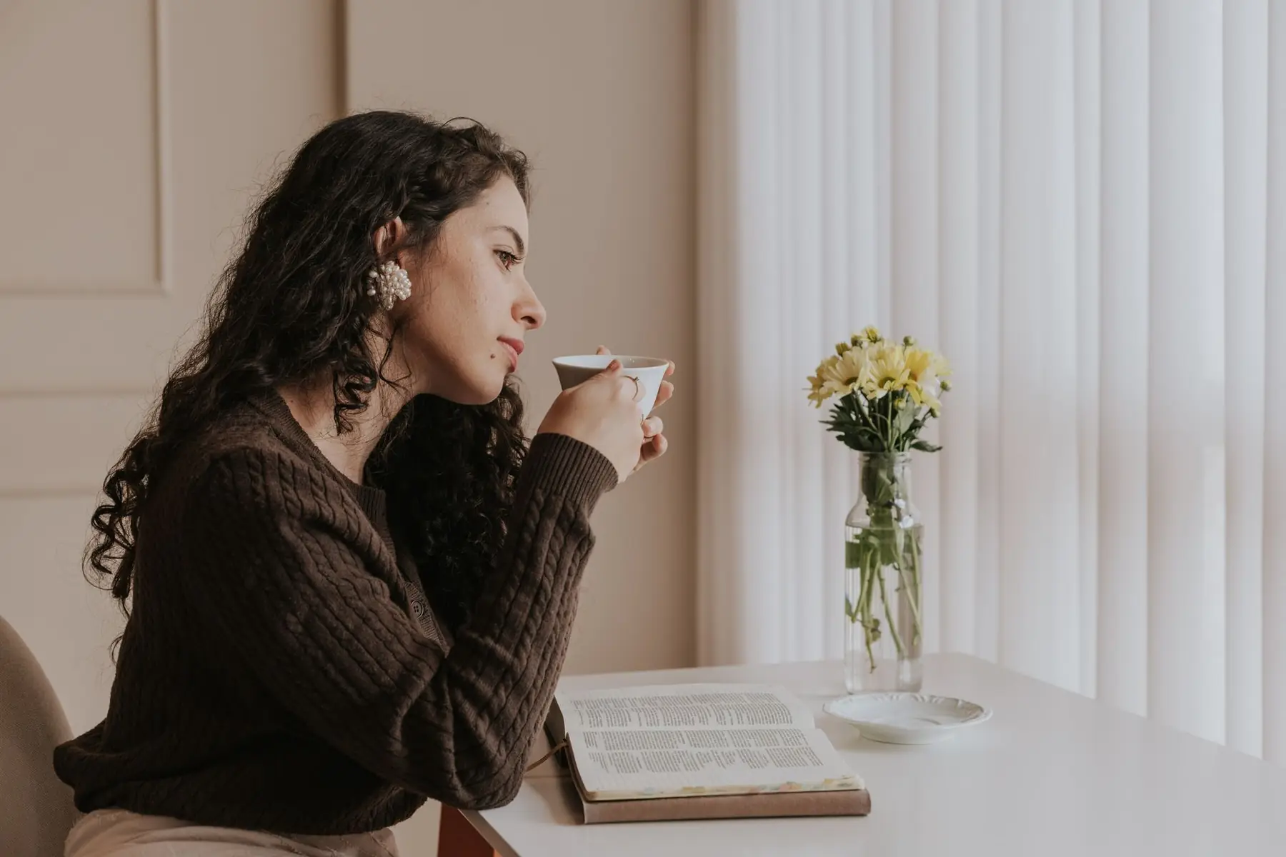 A woman relaxes with tea and a book by a bright window, embracing a