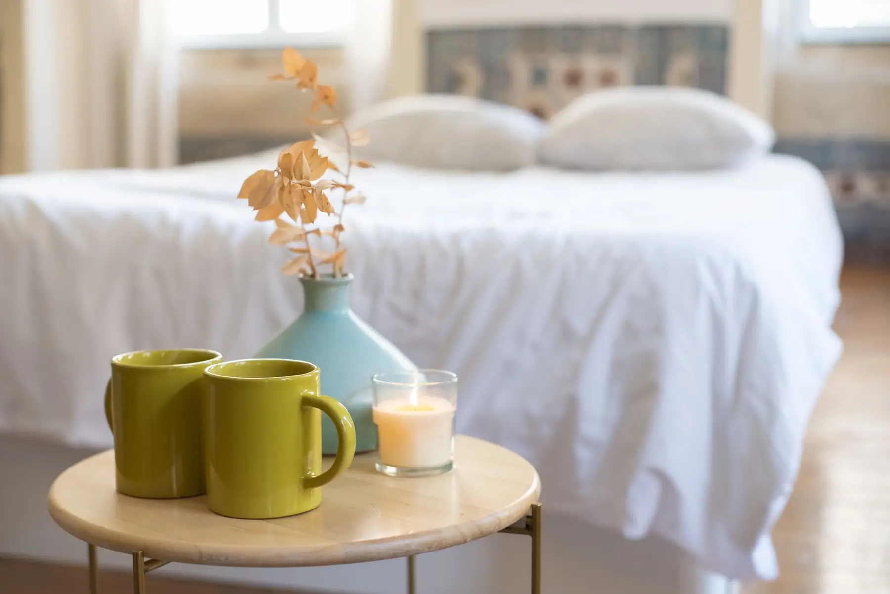 Inviting bedroom with a table setting featuring a candle, vase, and green mugs