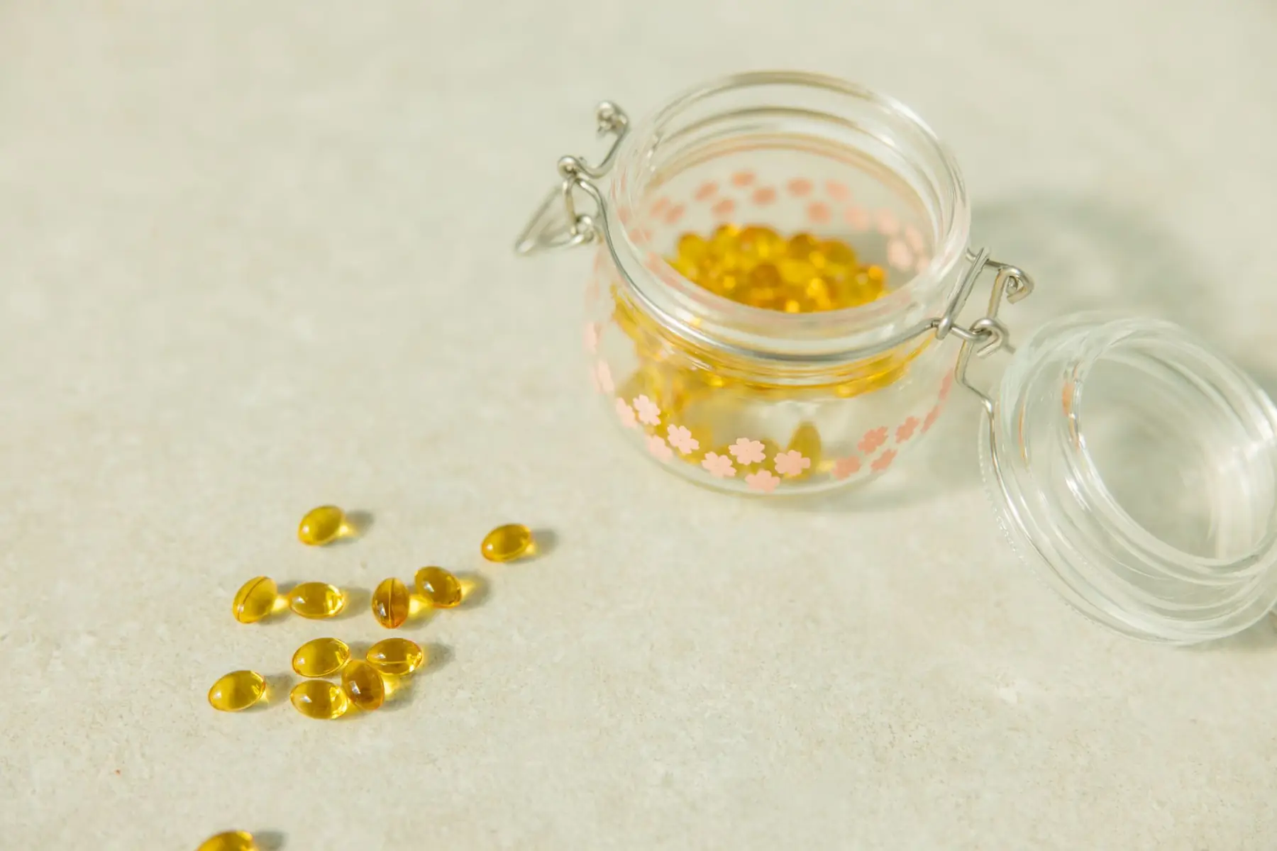 Close-up of open glass jar filled with yellow health capsules on light surface