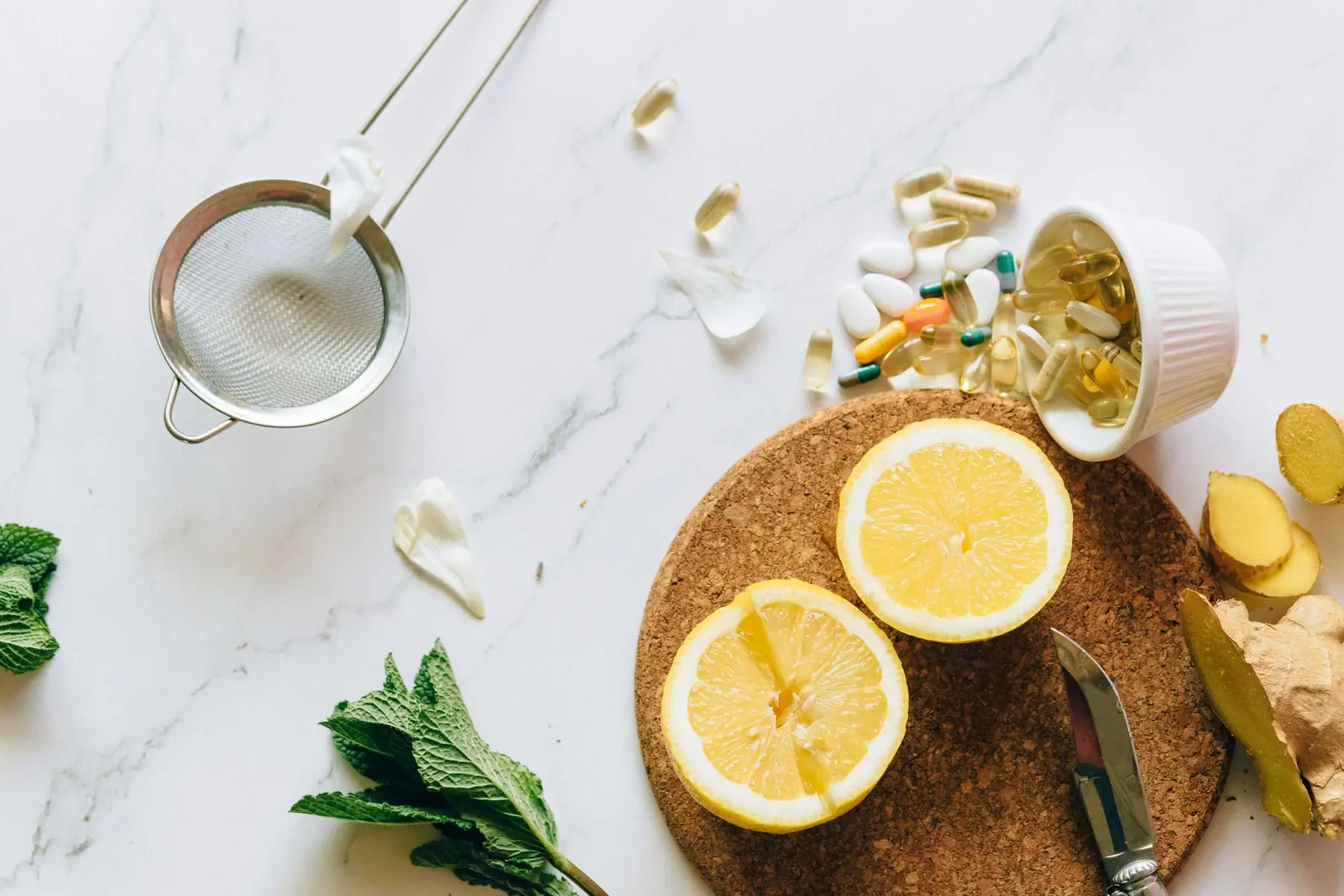 Flat lay of lemon, ginger, and supplements on a marble surface, illustrating natural remedies